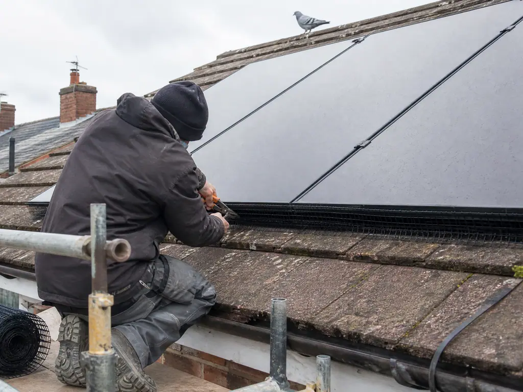 Installer clipping bird mesh around the edge of a solar panel array on a Birmingham roof